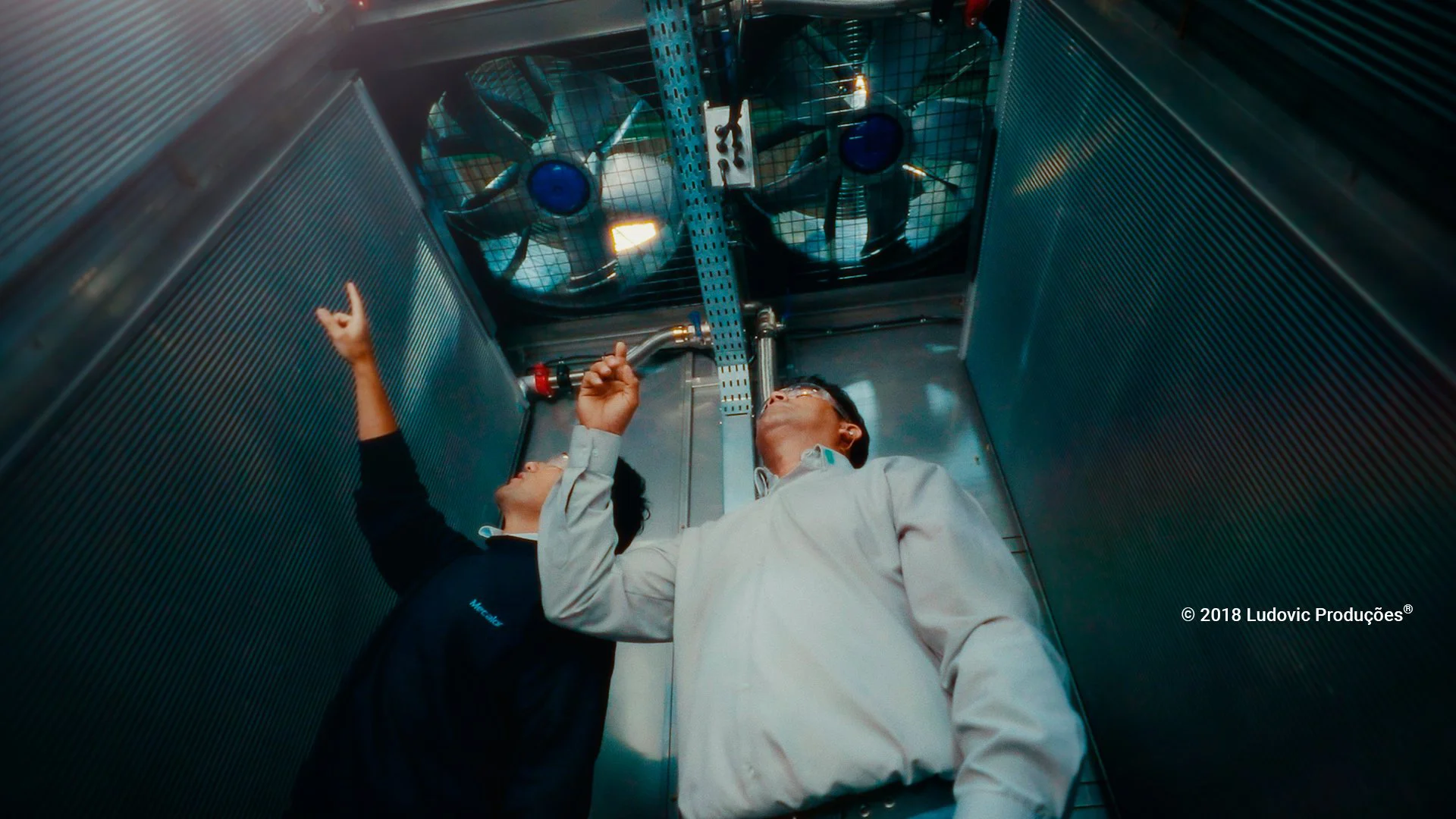 Profissionais com óculos de proteção inspecionam sistema de ventilação industrial, representando tecnologia e segurança em vídeo institucional