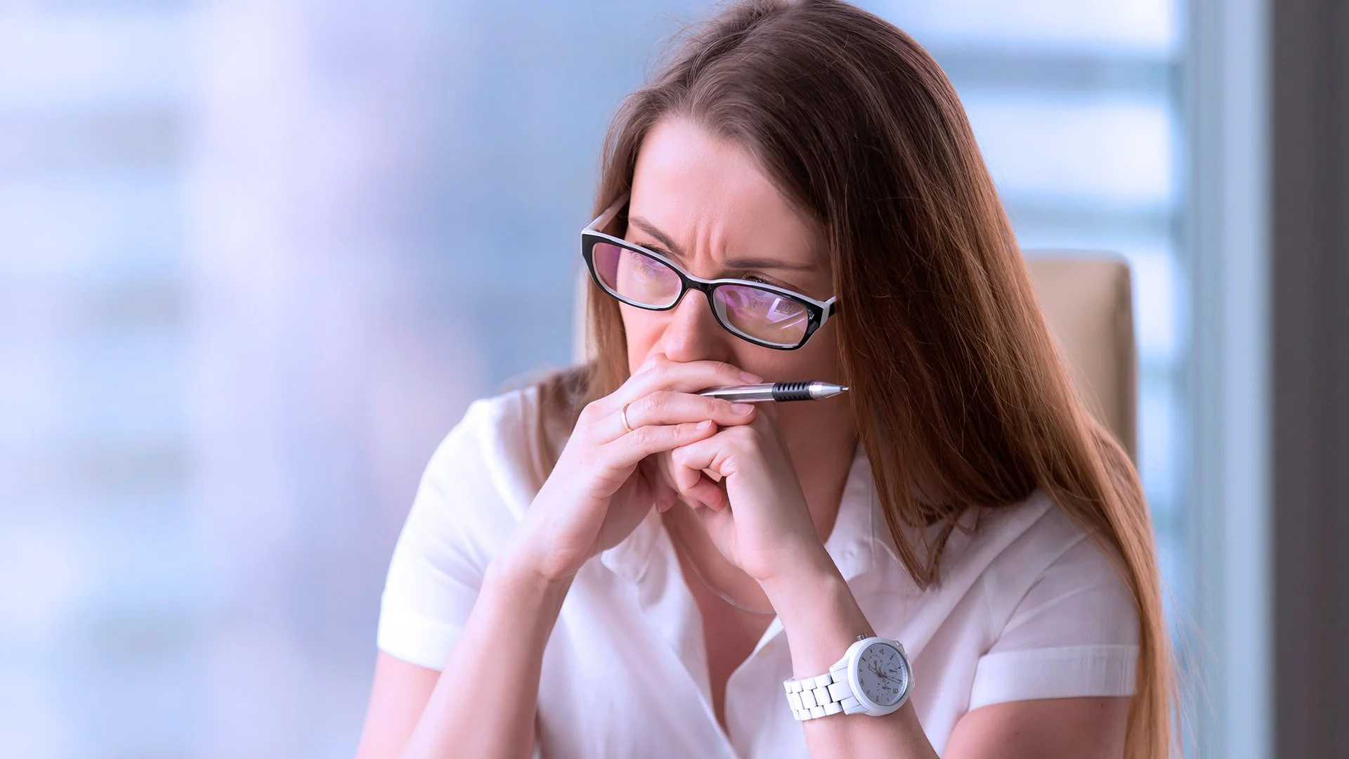Executiva com mãos apoiadas no queixo em gesto de escuta atenta, sentada em ambiente interno com fundo desfocado