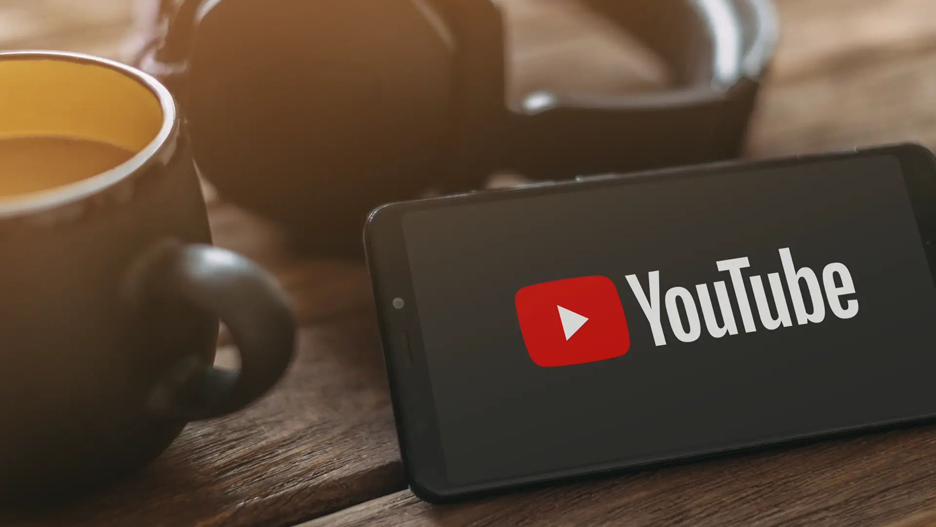 Celular com logo do YouTube sobre mesa ao lado de xícara de café, simbolizando divulgação acessível de empresas na plataforma.
