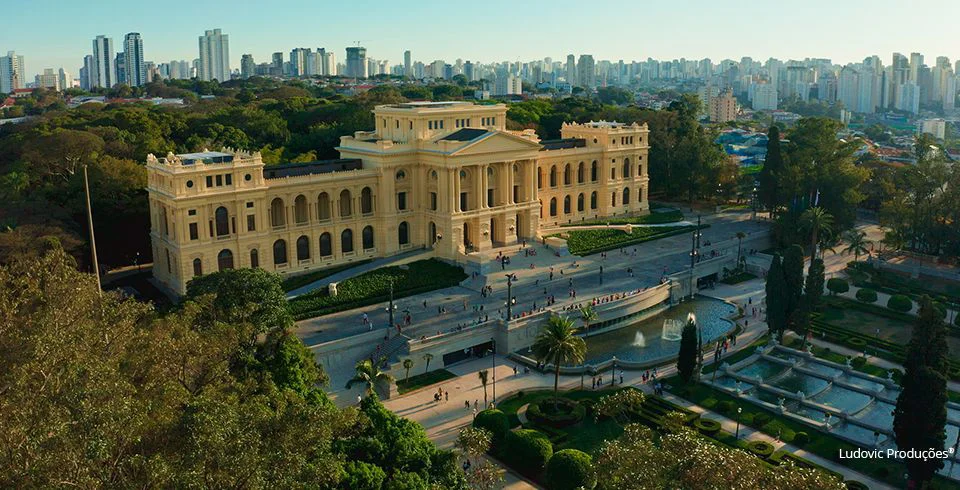 Museu do Ipiranga em São Paulo cercado por jardins e com skyline da cidade ao fundo, representando conexão entre história e identidade urbana em vídeo institucional para o Grupo Ultra.