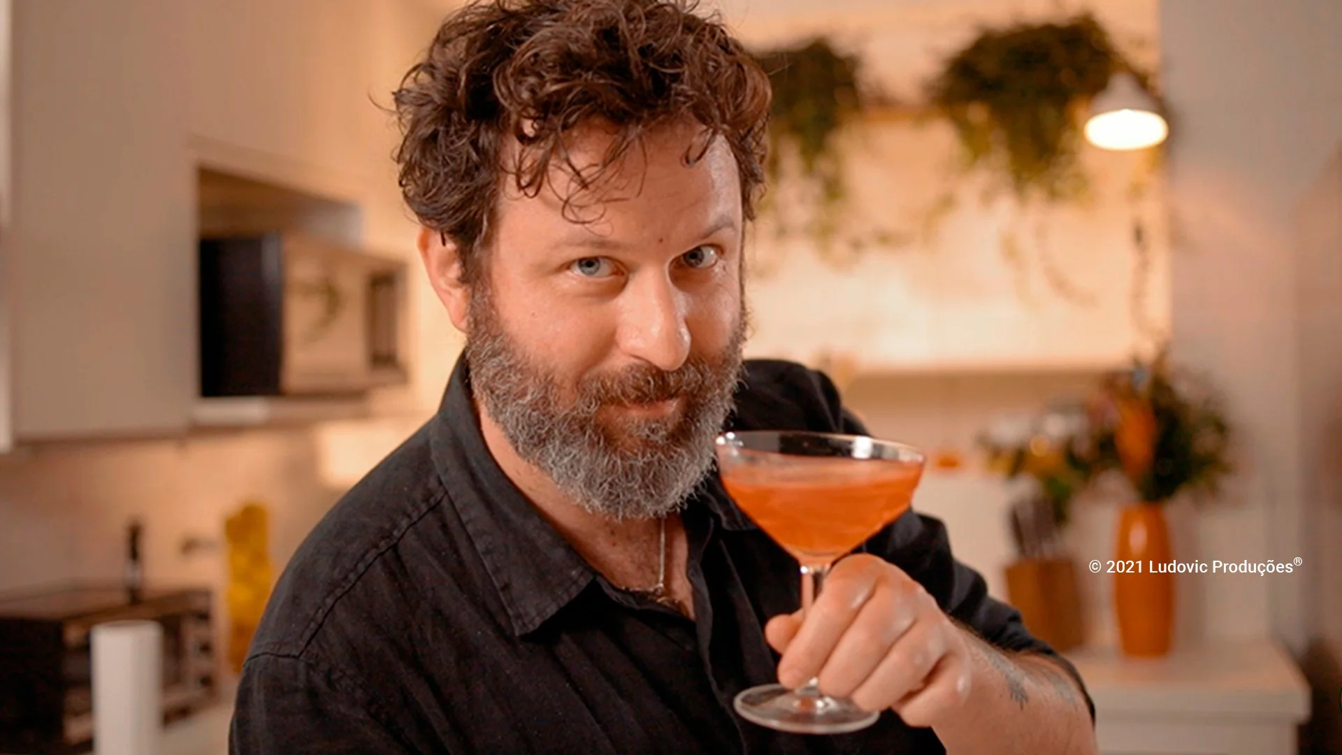 Ale D'Agostino segura taça em ambiente de cozinha moderna, simbolizando criatividade e expertise no episódio sobre drinks da websérie para a Mastercard.