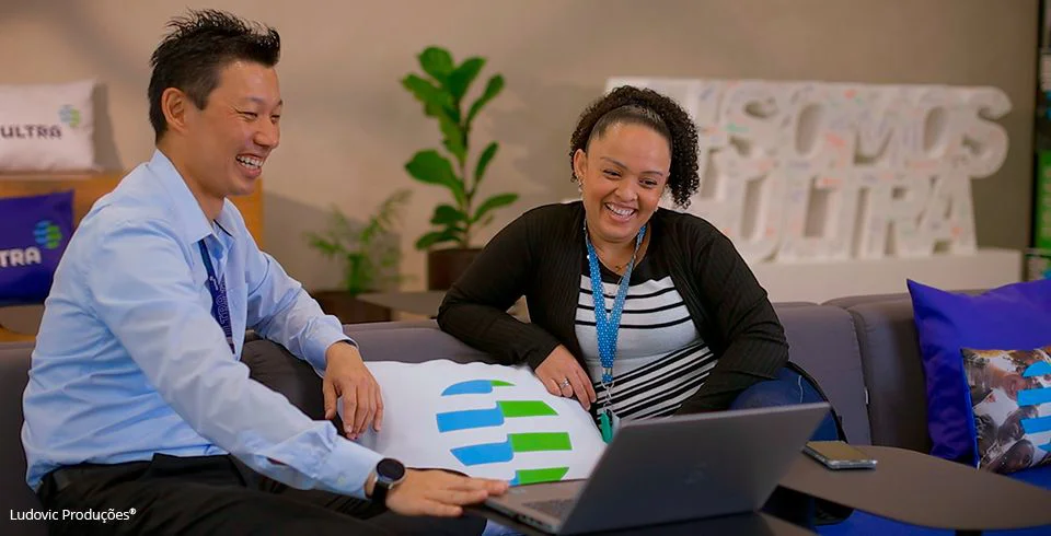 Dois profissionais em reunião com notebook em ambiente corporativo com almofadas, em cena de vídeo institucional produzido para o Grupo Ultra.