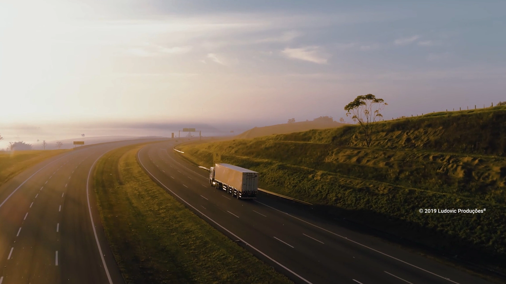 Cena aérea com caminhão de empresa de logística em estrada sinuosa, capturada por drone durante gravação institucional da Ludovic
